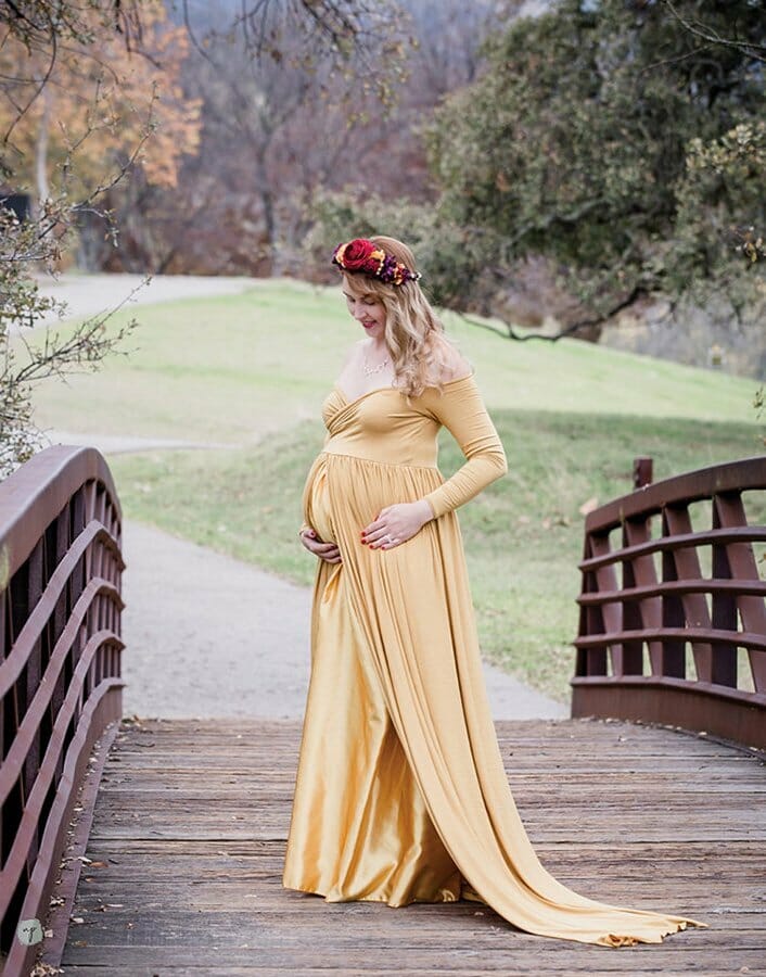 maternity photo of expectant mom looking at her belly and standing on a bridge in a gown